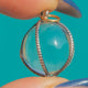 Rock Crystal orb pendant with Silver bands, held on blue background